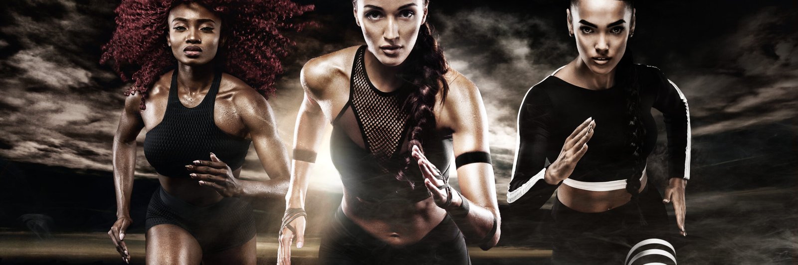 Three athletic women running together in a dramatic, smoky setting, symbolizing strength and unity in fitness.