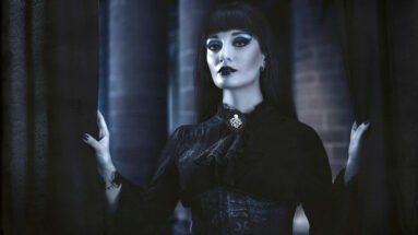 Gothic woman in dark Victorian-inspired attire, standing ominously behind a curtain with a haunting expression.