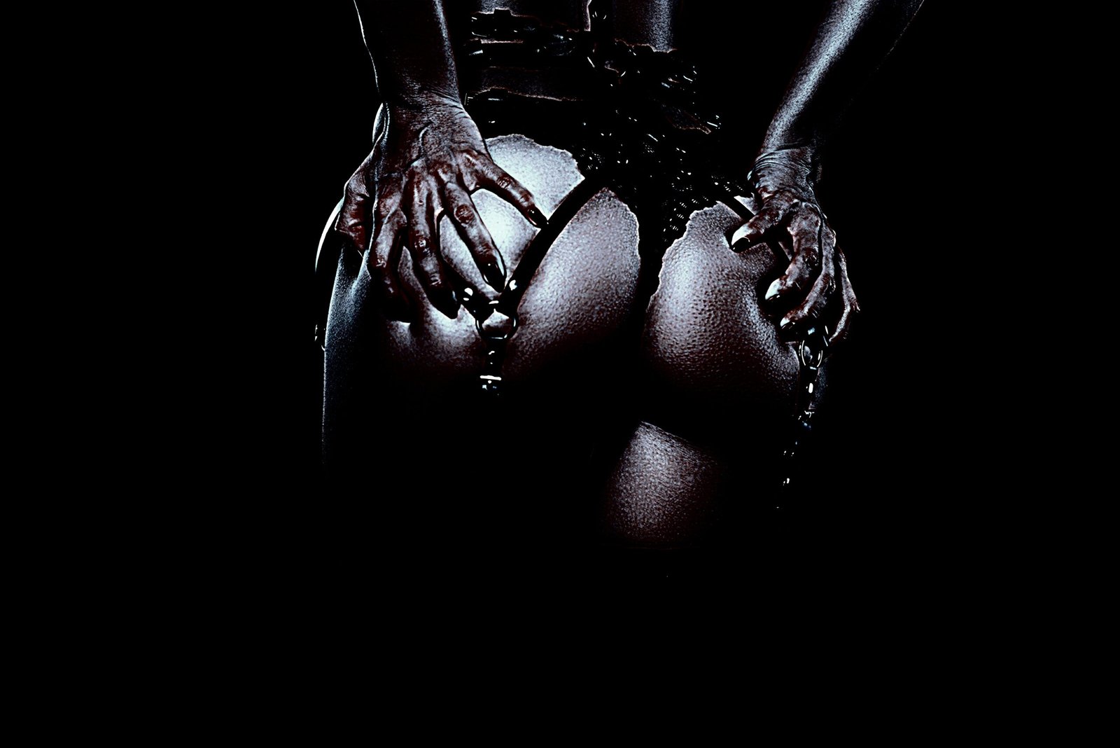 Close-up of a person wearing tight black leather pants with a chain belt, shown from the back.