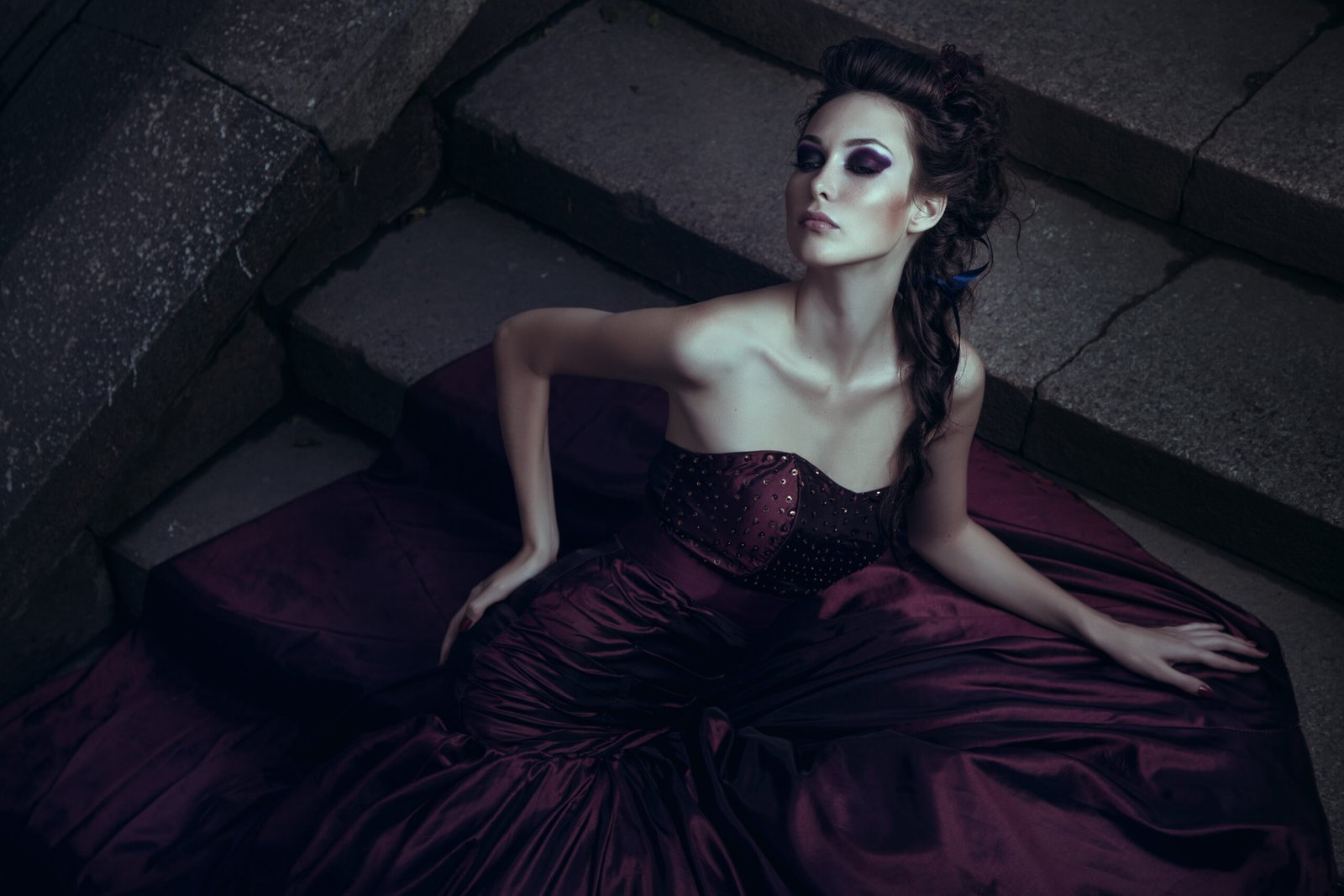Gothic woman in a deep purple satin gown, reclining gracefully on stone steps in a dramatic, moody setting.