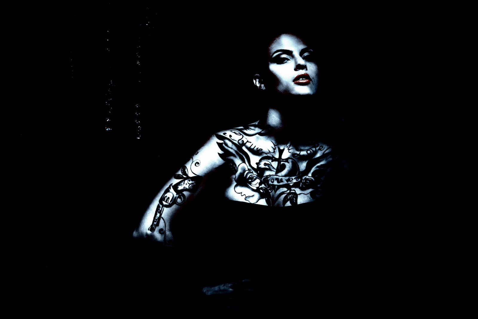 Woman with extensive gothic tattoos on her chest and arms, posing against a dark background with a confident expression.