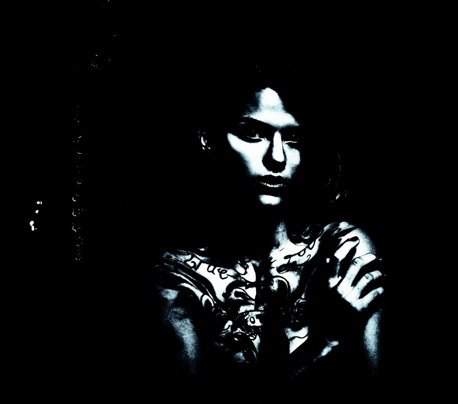 Woman with gothic chest tattoos standing with her arms crossed in a dark, shadowy environment.