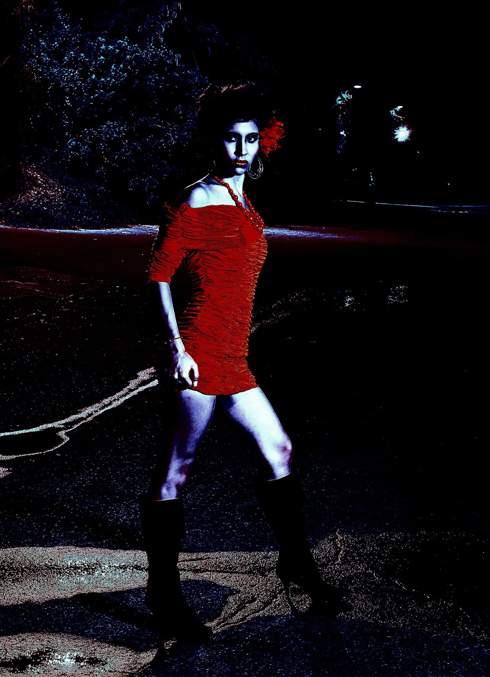 Woman in a red dress walking confidently at night, with a flower in her hair and a determined expression.