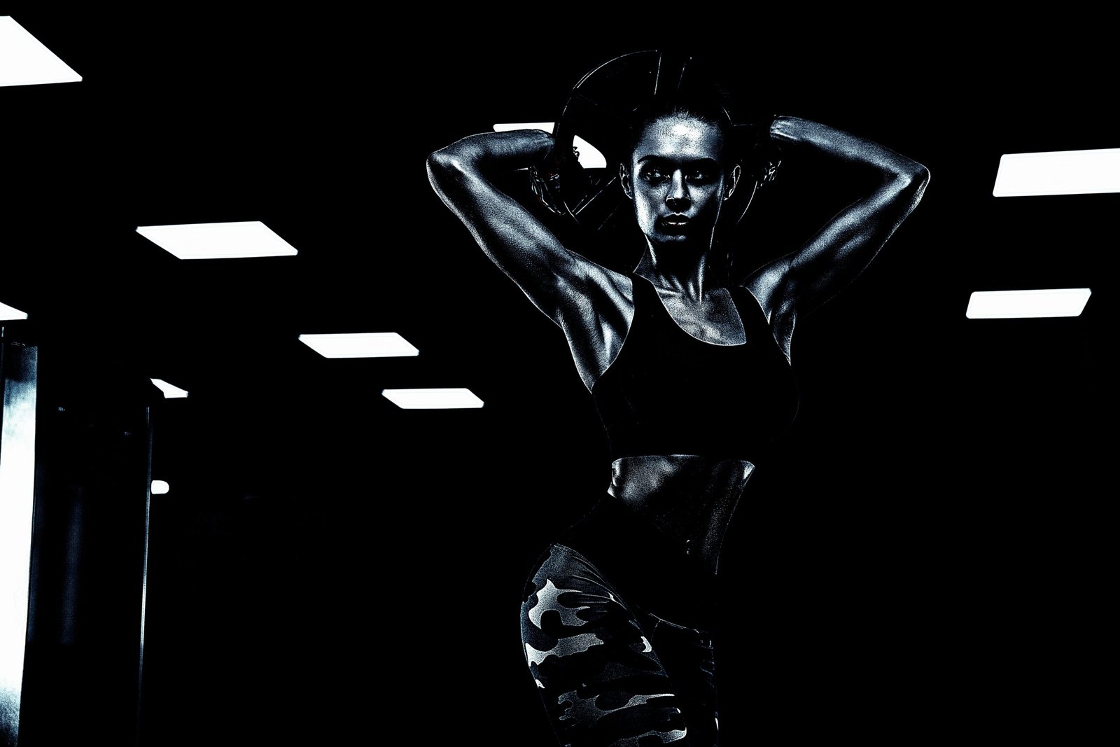 Fit woman lifting a weight plate above her head, with intense lighting creating a dramatic effect.
