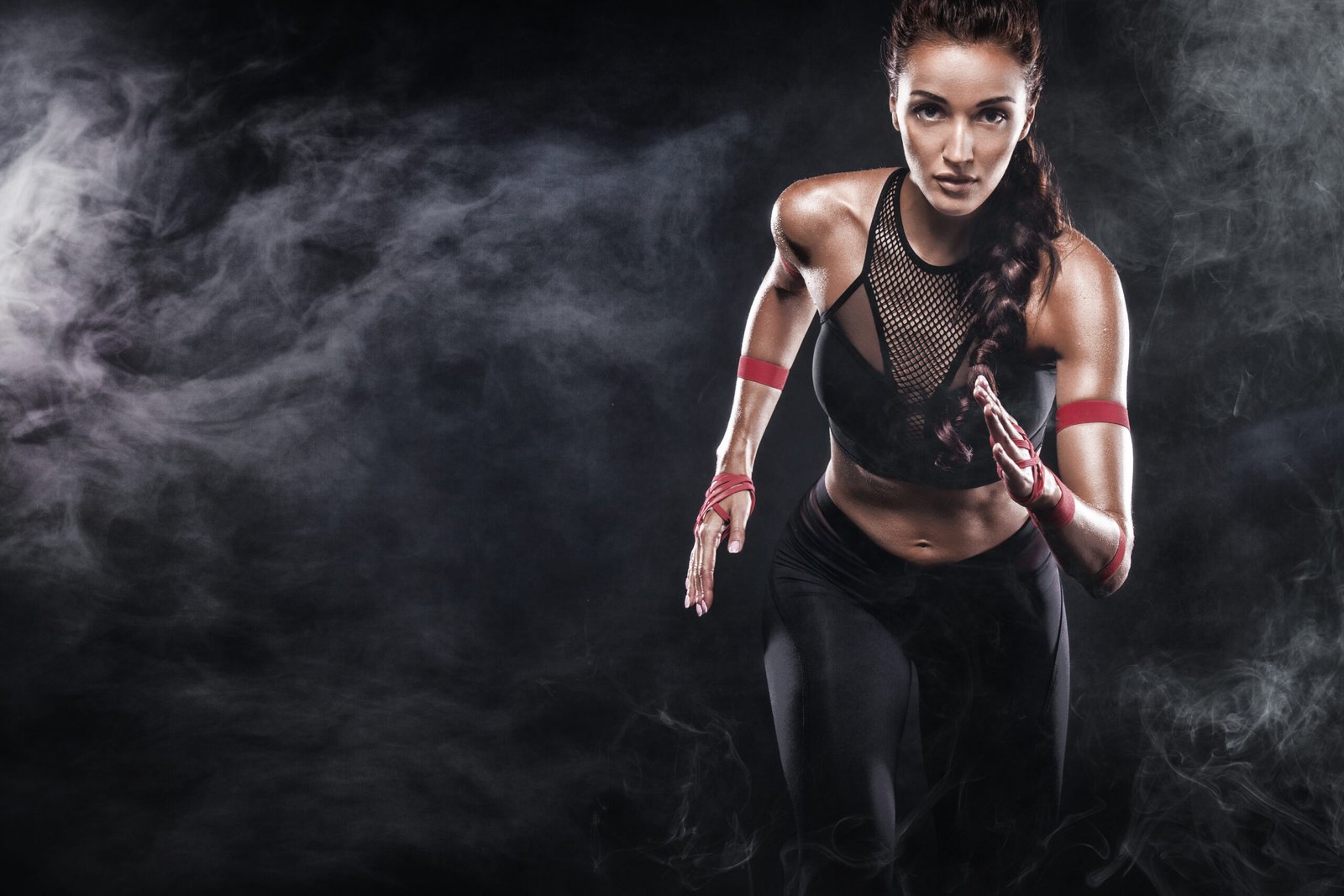 Fit woman in a black mesh sports bra running through a dark, foggy environment.