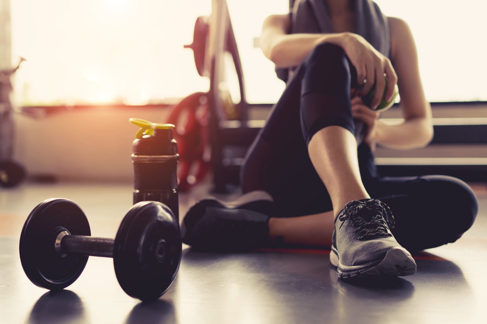 Woman in a gym sitting next to dumbbells and a water bottle after an intense workout.