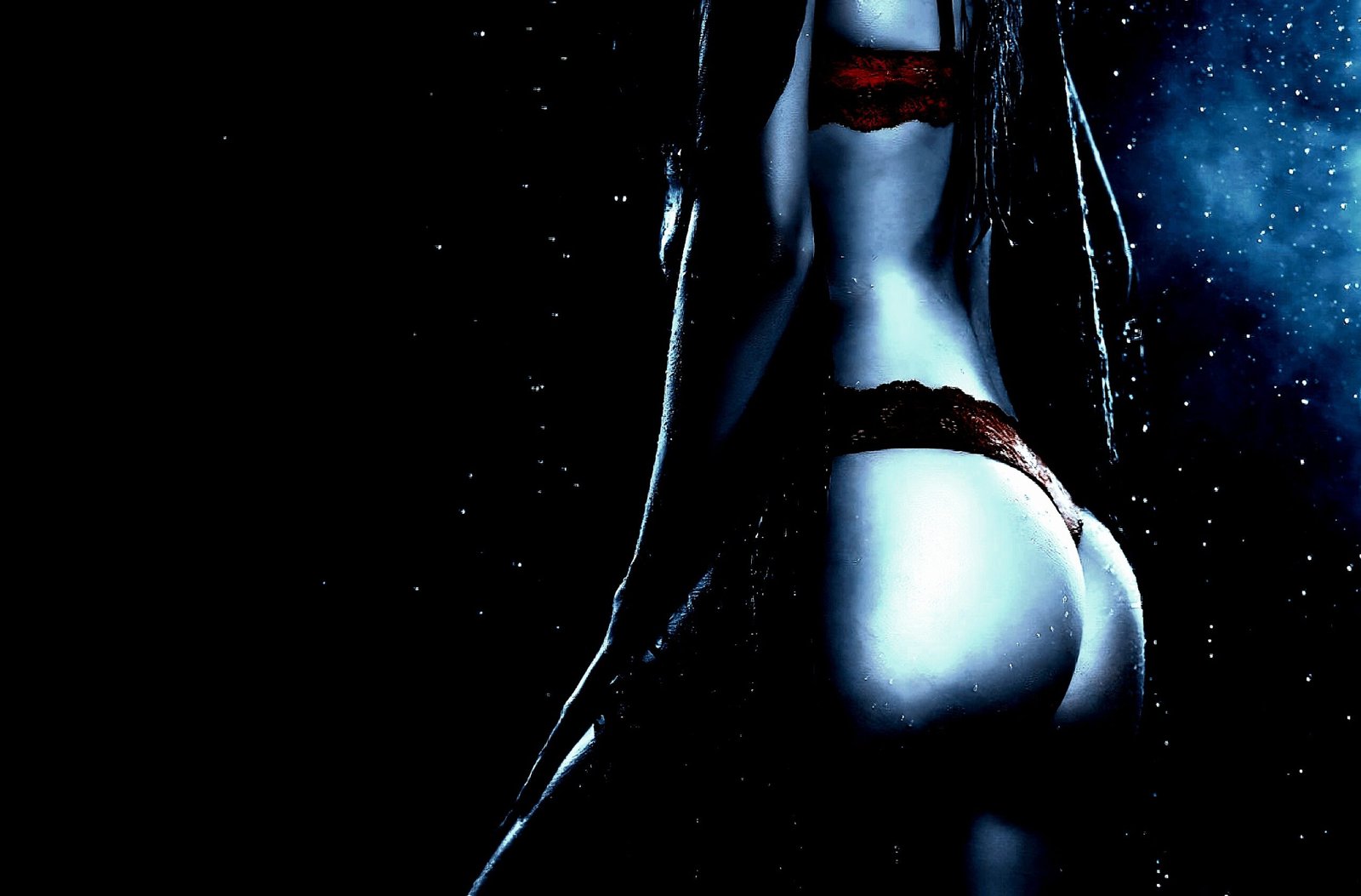 Close-up of a person wearing tight black latex pants and dark nail polish, with hands resting on their buttocks.