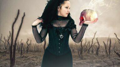 A gothic woman in a black corset holding a skull emitting red light and smoke, in a barren landscape with twisted, leafless trees.