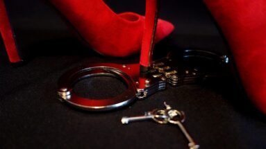 Red high heel resting next to a pair of handcuffs and keys on a black surface.