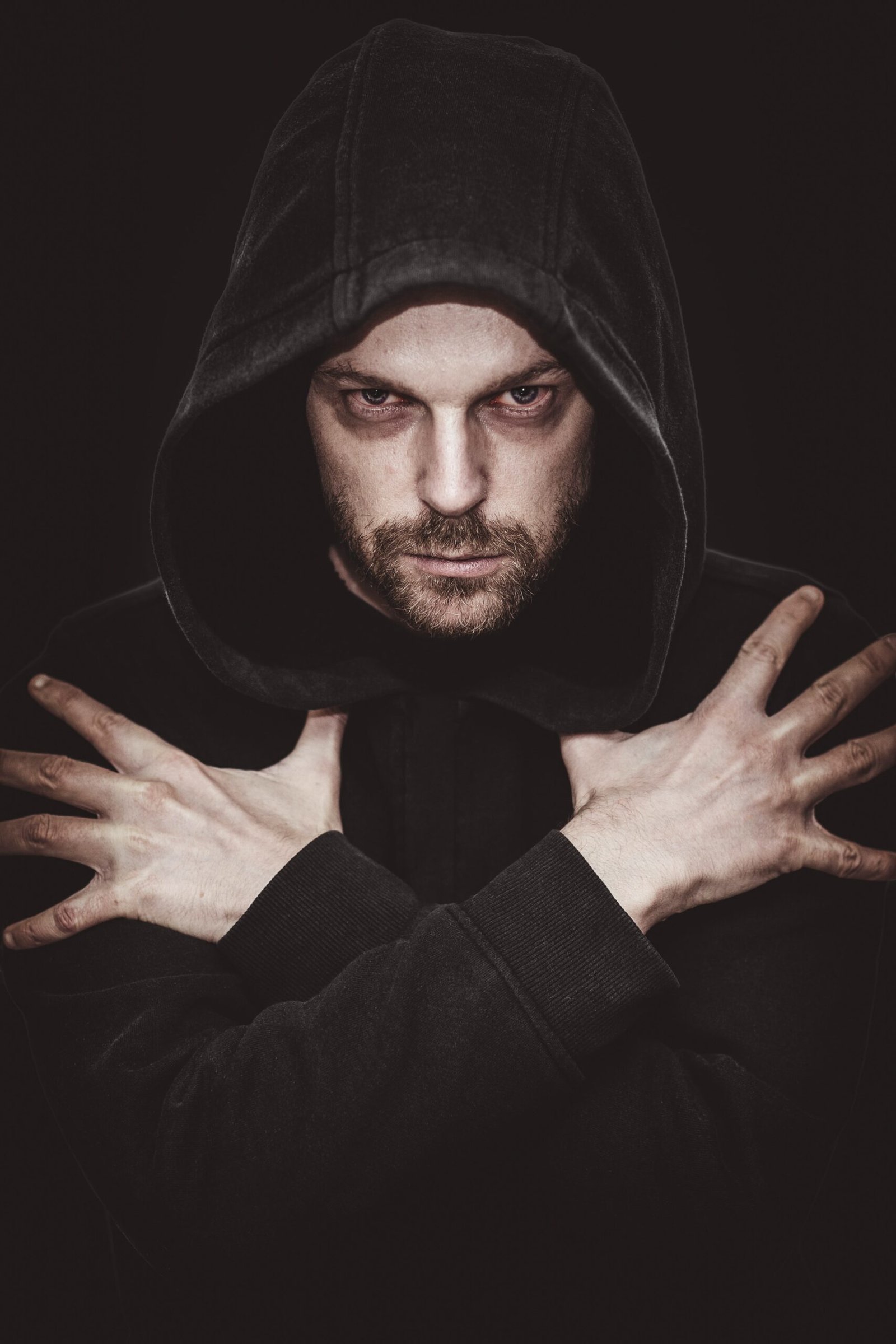 Brooding man with intense gaze, wearing a dark hoodie and crossing his arms in a vampire-like manner.