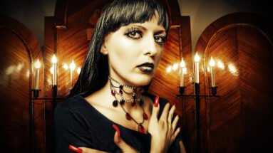 Gothic woman with dark makeup and spider web earrings, wearing a strappy top and choker necklace in a black-and-white photo.