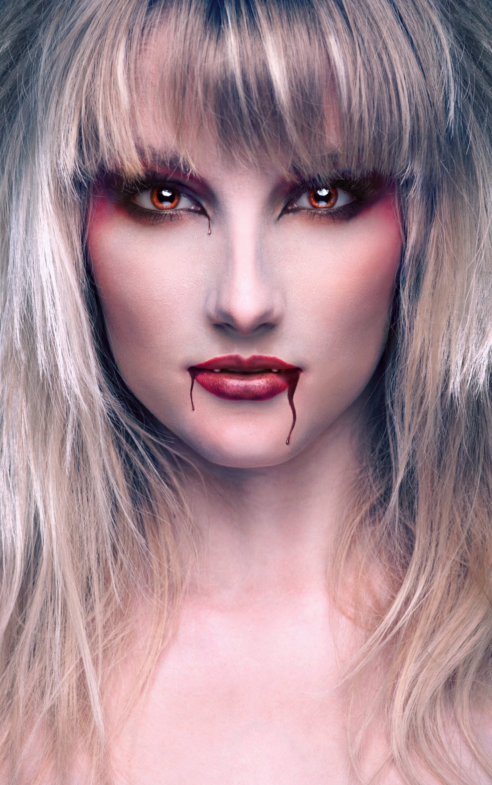 Blonde female vampire with blood dripping from her lips, piercing eyes, and a haunting expression.