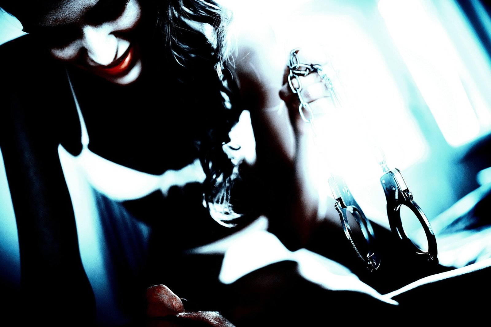 Woman in white bra holding handcuffs, with a shadowed man on a bed in the background.