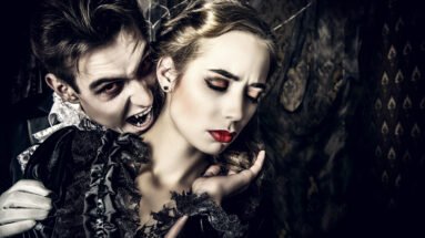 A male vampire with fangs biting a woman's neck, both dressed in gothic attire with dark, dramatic makeup in a haunting atmosphere.