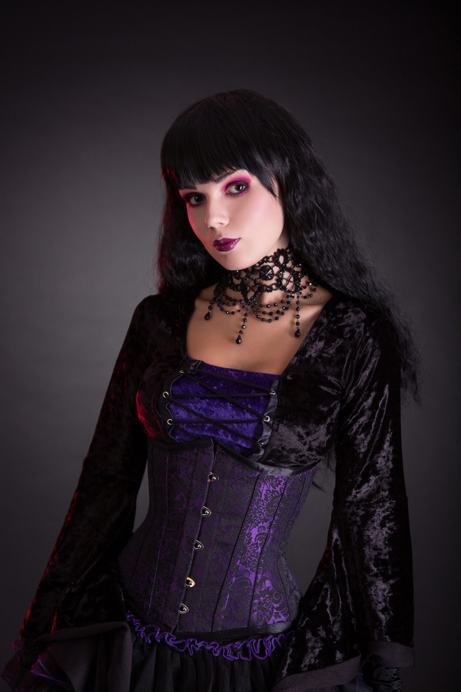 Gothic woman in a black and purple corset with intricate lace details, standing confidently against a dark background, highlighting gothic elegance.