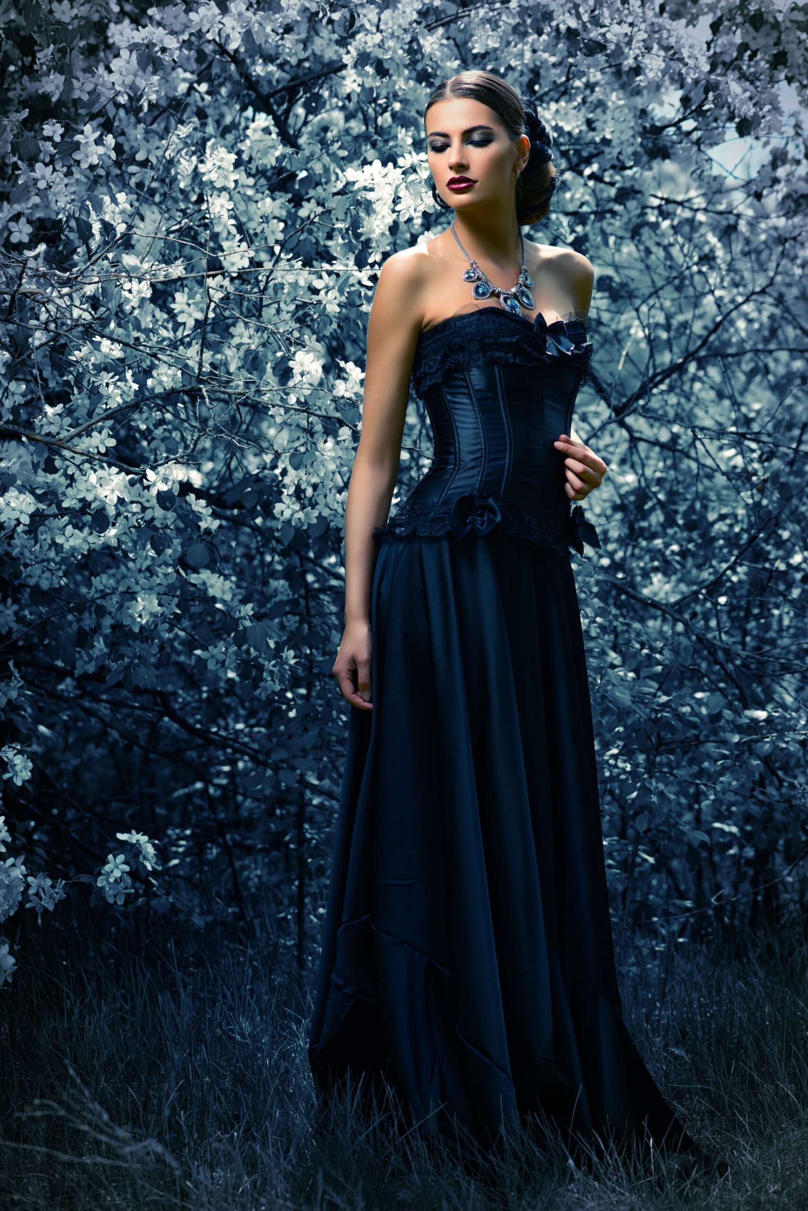 Gothic woman in a long black dress with a corset, standing in a blooming dark forest, evoking a mysterious and ethereal atmosphere.