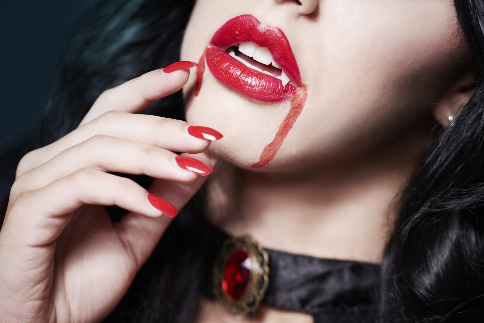 Close-up of a woman’s lips and red nails, with vampire fangs visible and blood dripping from her mouth, evoking a seductive vampire aesthetic.