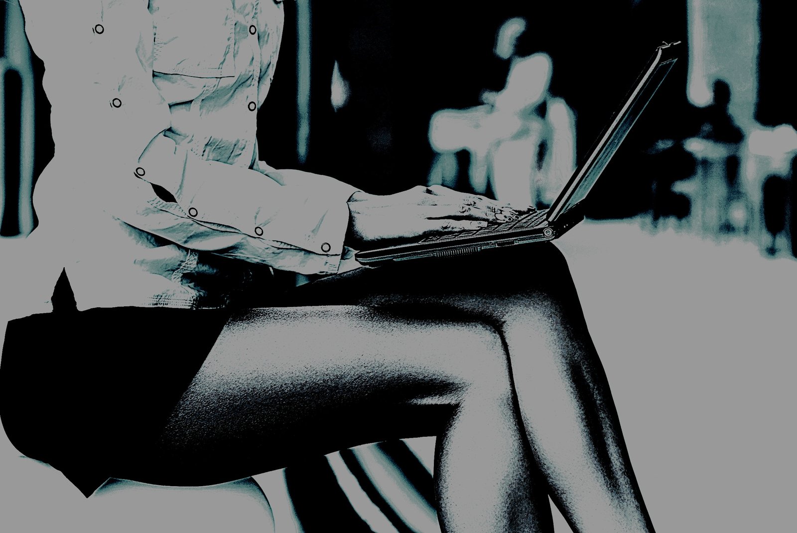 Close-up image of a woman's crossed legs in stockings, typing on a laptop in a modern office setting.
