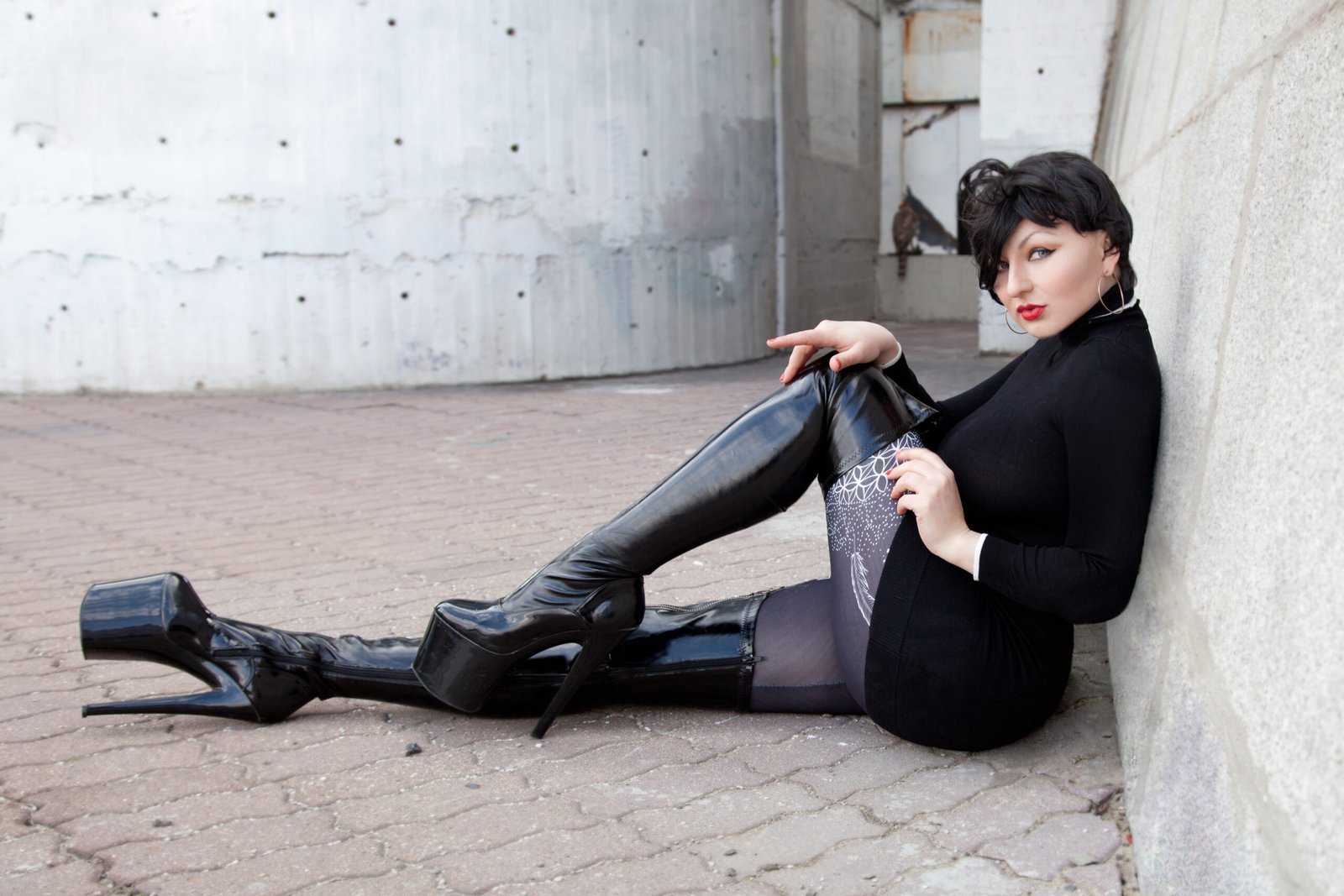 Woman lounging on the ground in black leather boots and dark attire, showcasing edgy street style with an alternative flair.