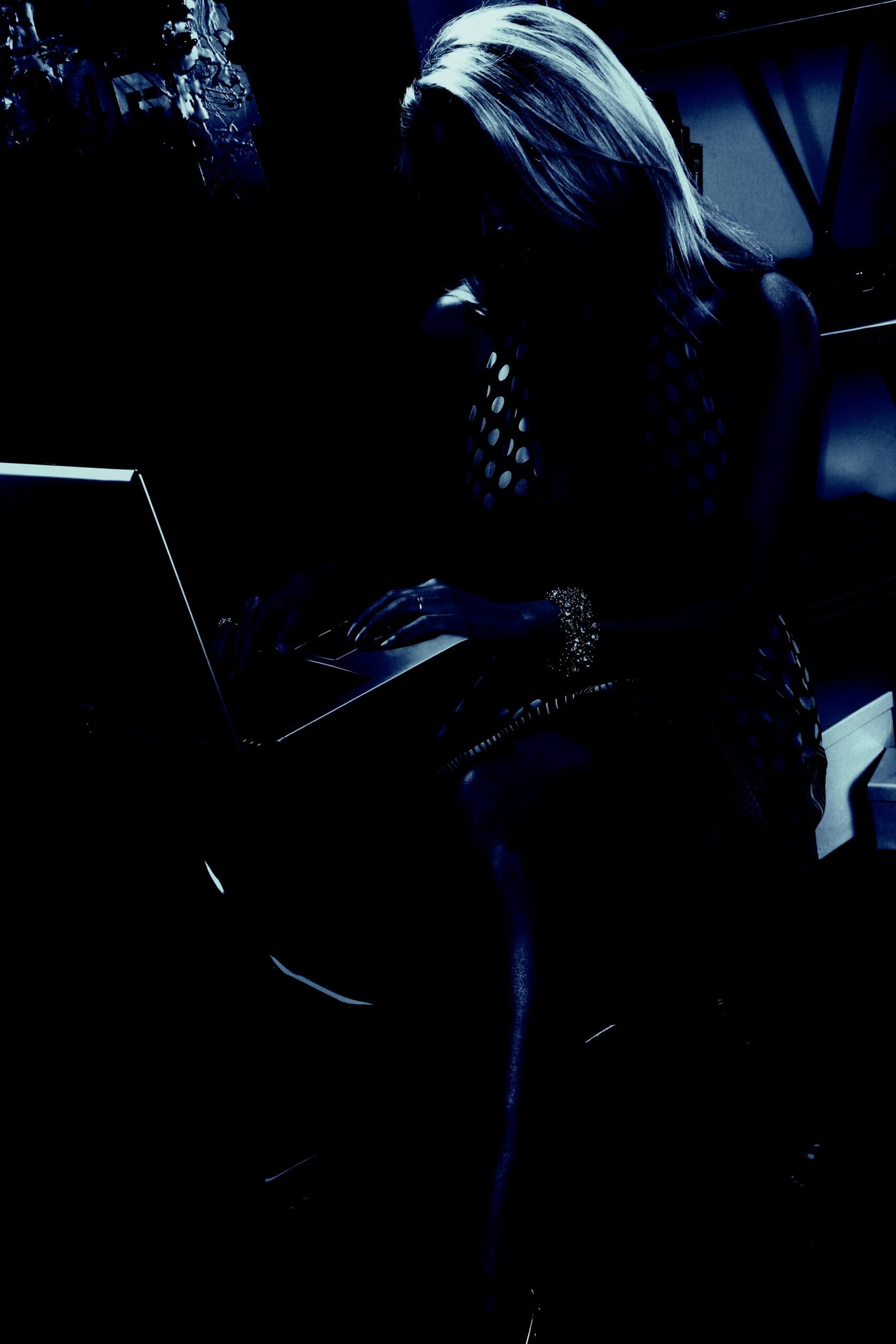 Mysterious silhouette of a woman working on a laptop in a dark, dimly lit environment, creating an enigmatic and shadowy scene.