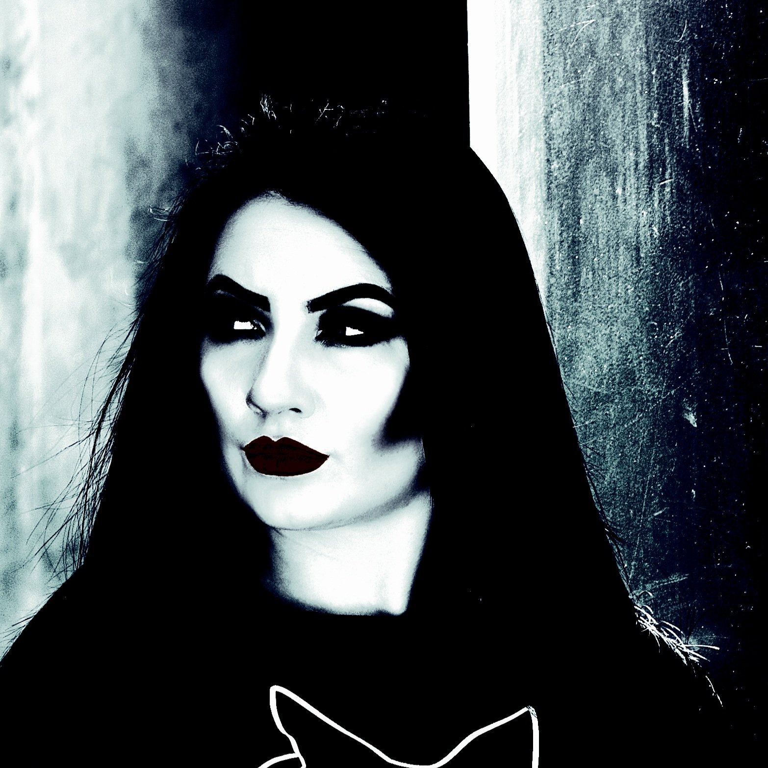 Close-up of a woman with dramatic makeup, dark hair, and red lipstick against a dark, shadowy background.