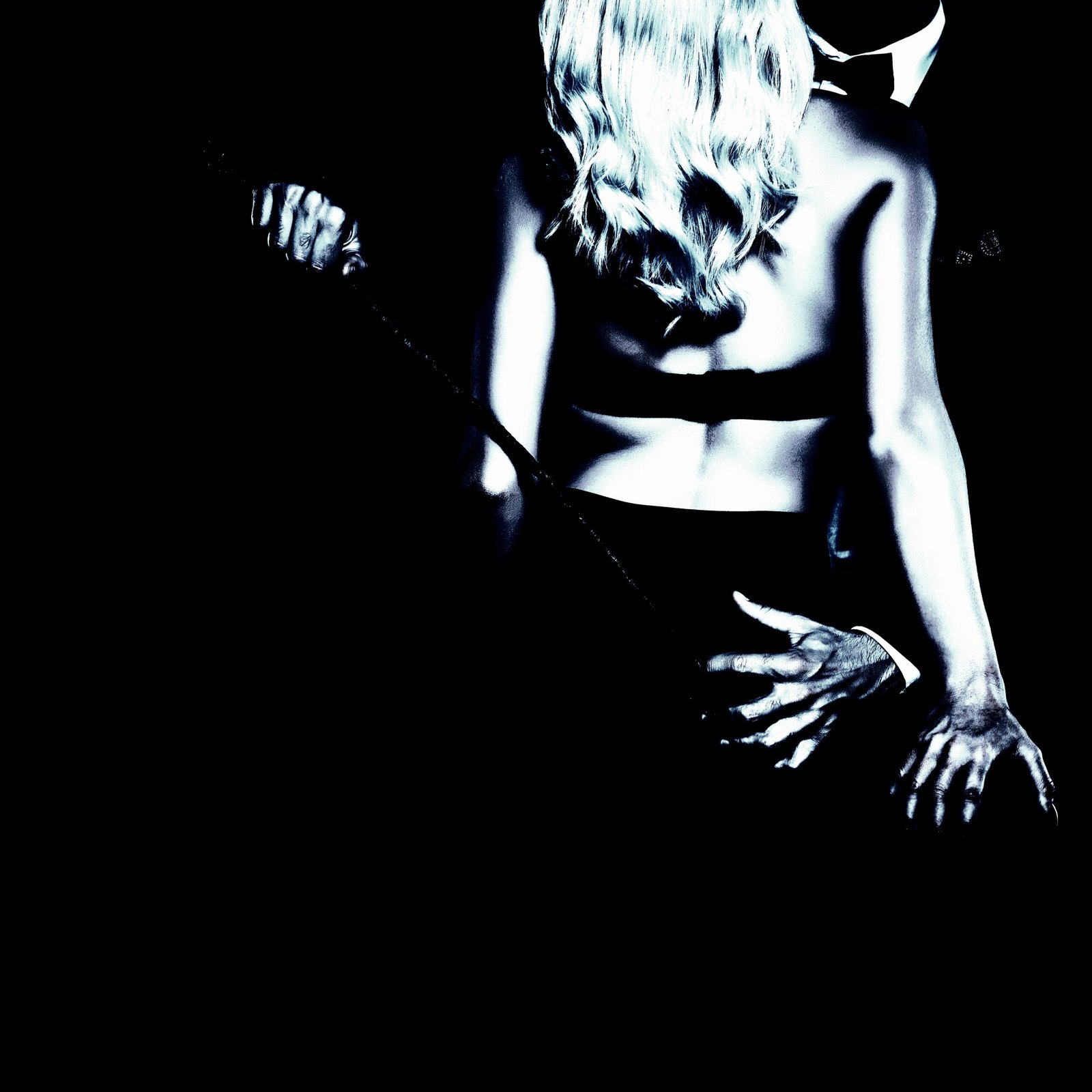 Couple in an intimate embrace, the woman in lingerie and the man in a suit, holding a whip.