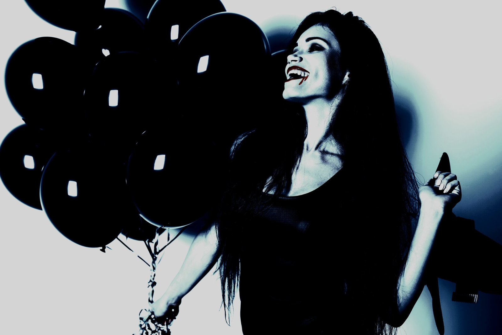 Smiling woman with long dark hair holding black balloons, wearing fangs, and dressed in a black outfit.