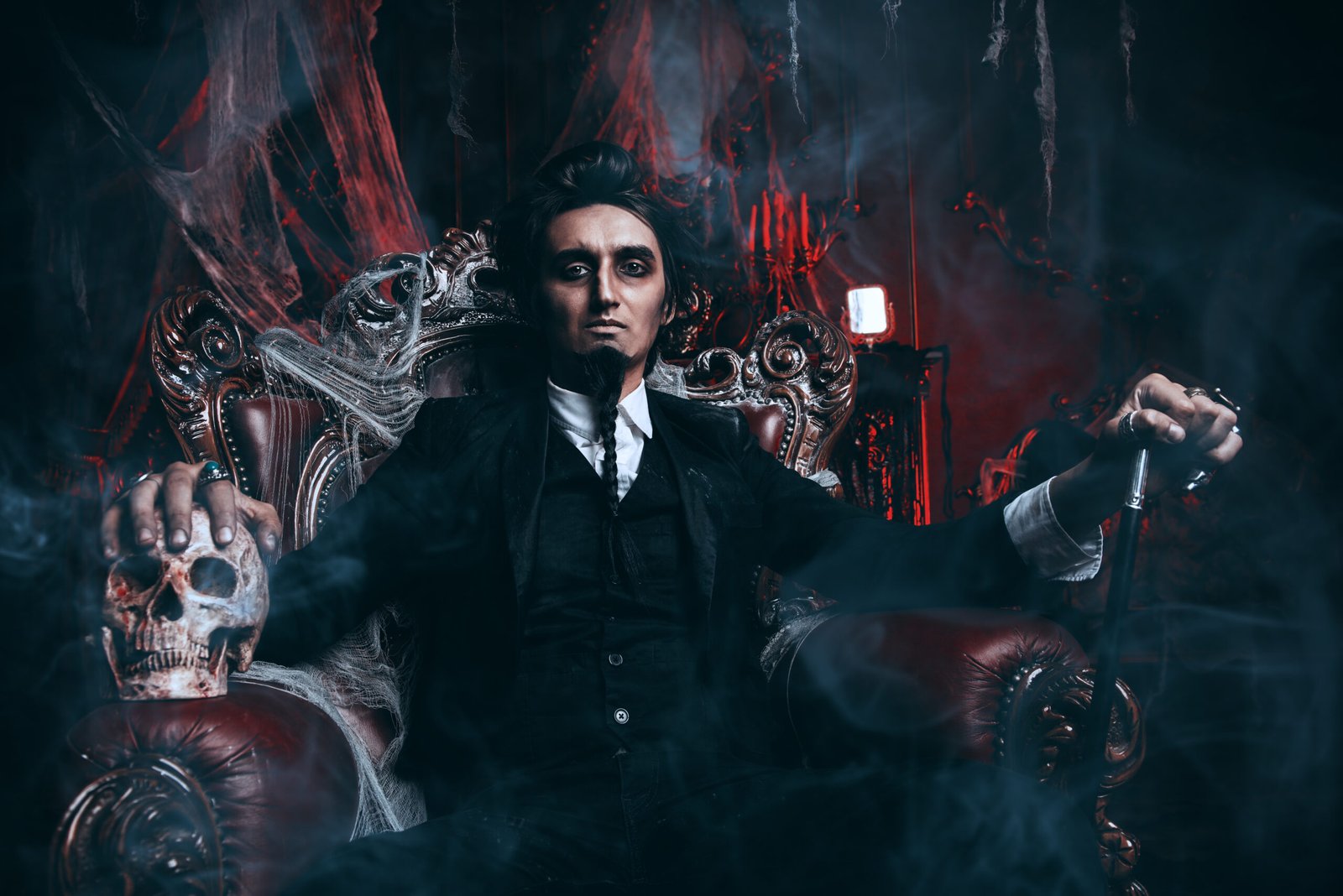 A male vampire with fangs biting a woman's neck, both dressed in gothic attire with dark, dramatic makeup in a haunting atmosphere.