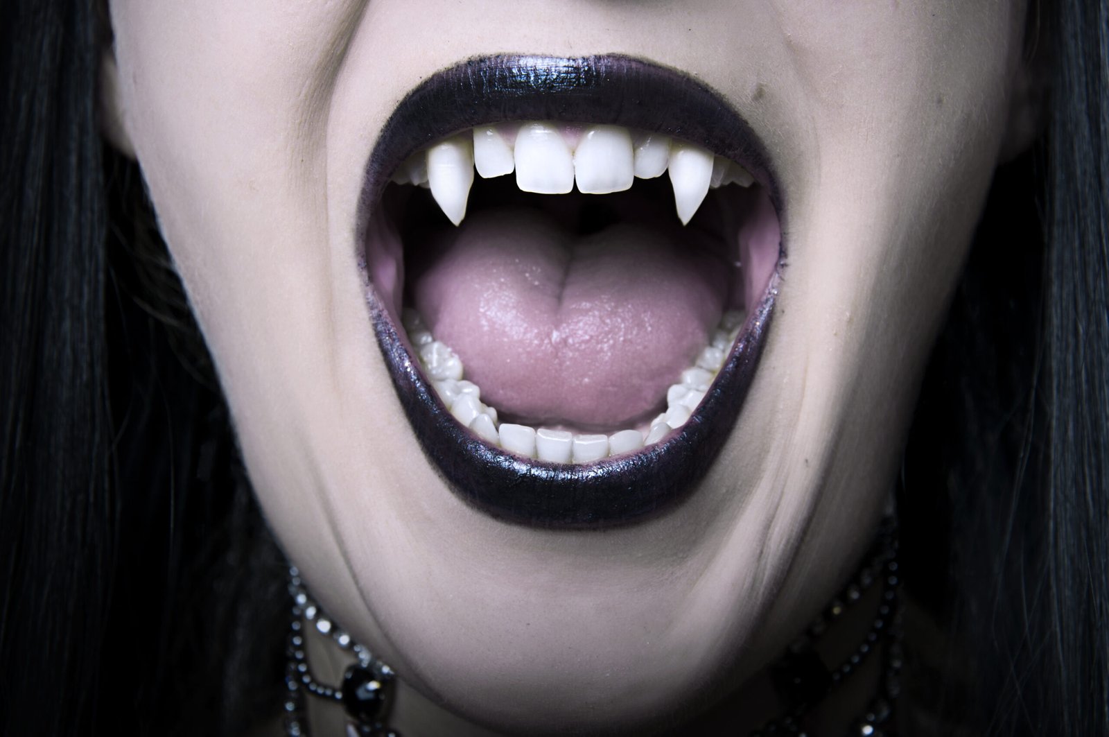 Close-up of a vampire's mouth with sharp fangs and dark lipstick.