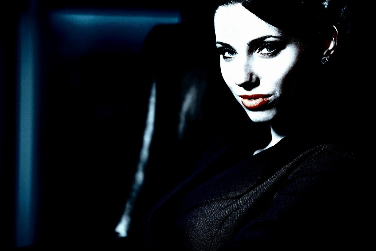 Moody portrait of a woman with red lips, shown in dark lighting, evoking a mysterious atmosphere.