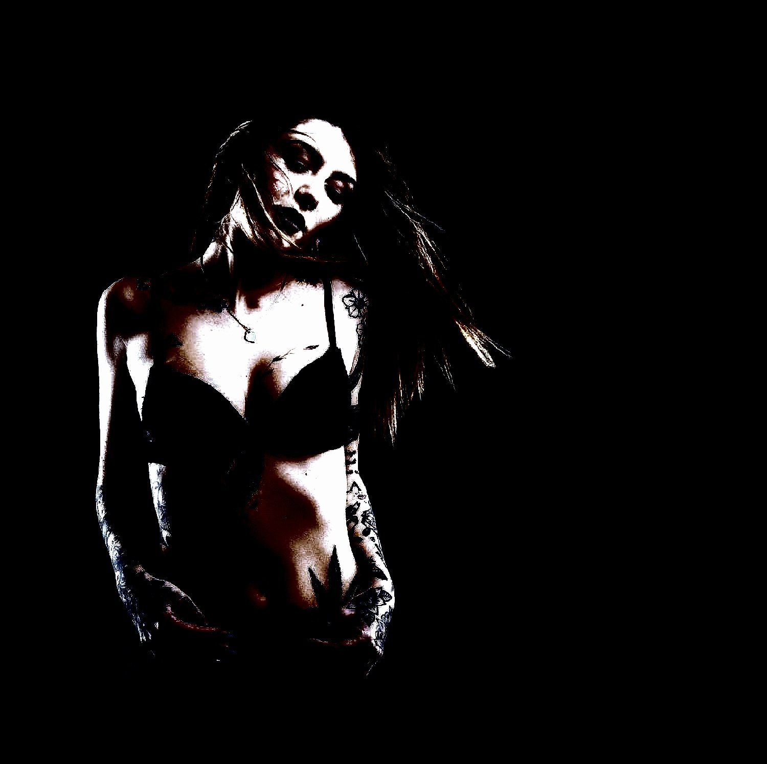 Sensual gothic woman in black lingerie, showcasing tattoos in a dark, minimalist setting. 