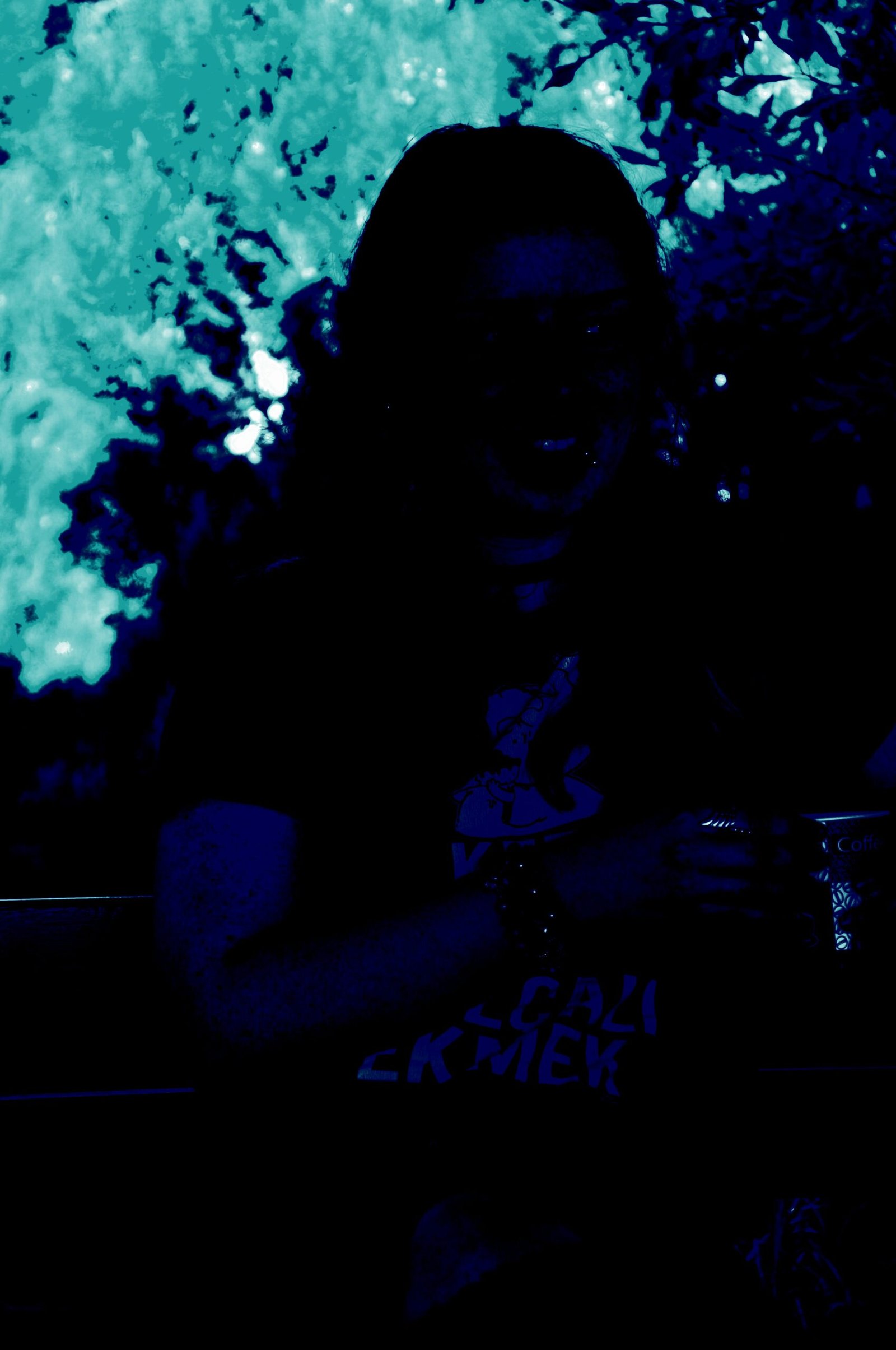 Shadowed woman with long hair holding a coffee cup, illuminated by cool blue tones, blending a casual vibe with dark lighting. 