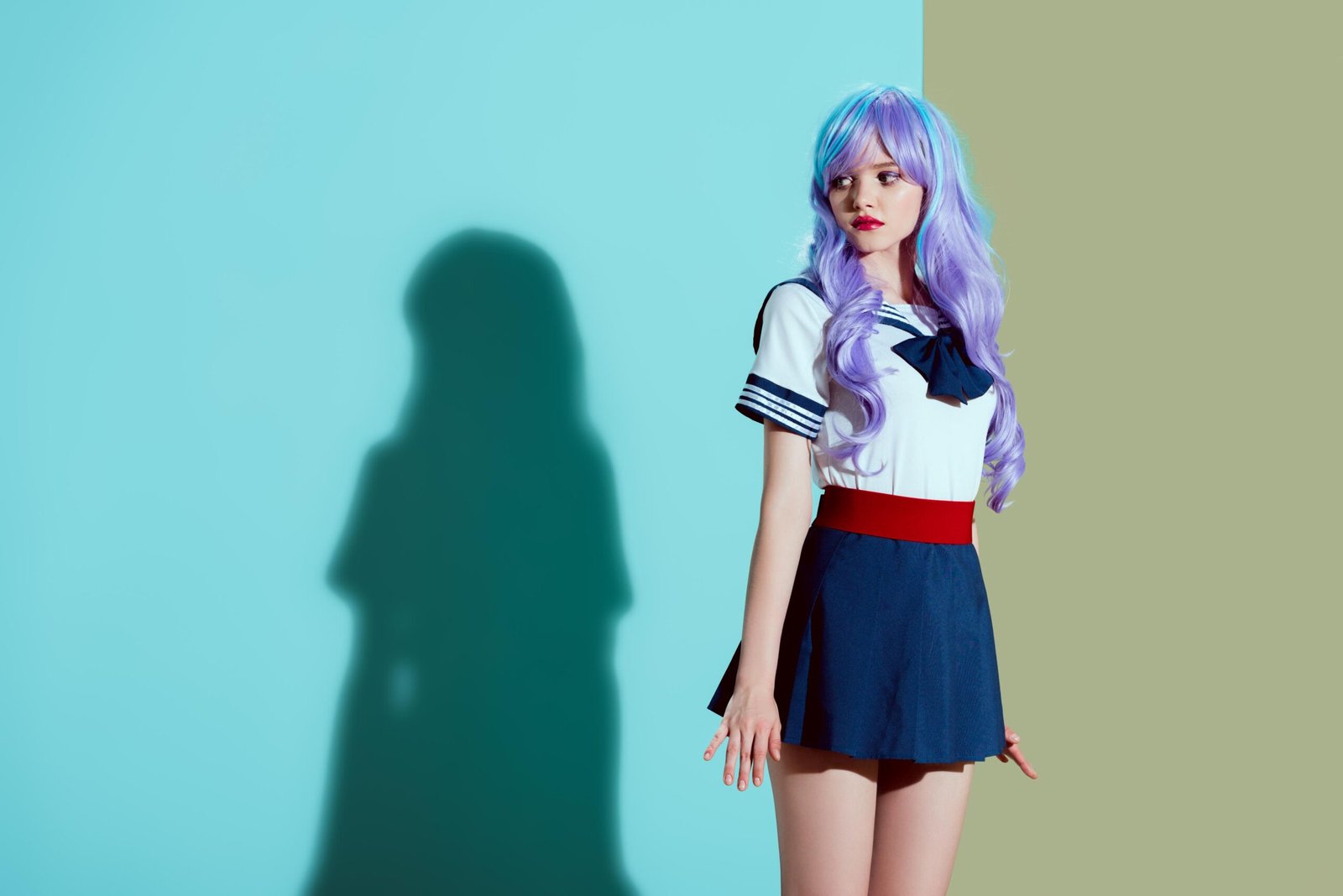 A cosplayer with purple hair in a sailor-inspired uniform, standing against a bright two-tone backdrop, with a colorful, dreamy atmosphere.