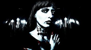 Close-up of a woman with dark lipstick and layered necklaces against candlelight, embodying a classic gothic look and somber mood.