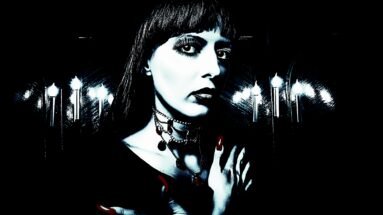 Close-up of a woman with dark lipstick and layered necklaces against candlelight, embodying a classic gothic look and somber mood.