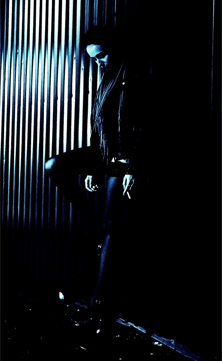 Woman smoking in a leather jacket against a metallic wall, surrounded by shadows for a gritty and moody look.