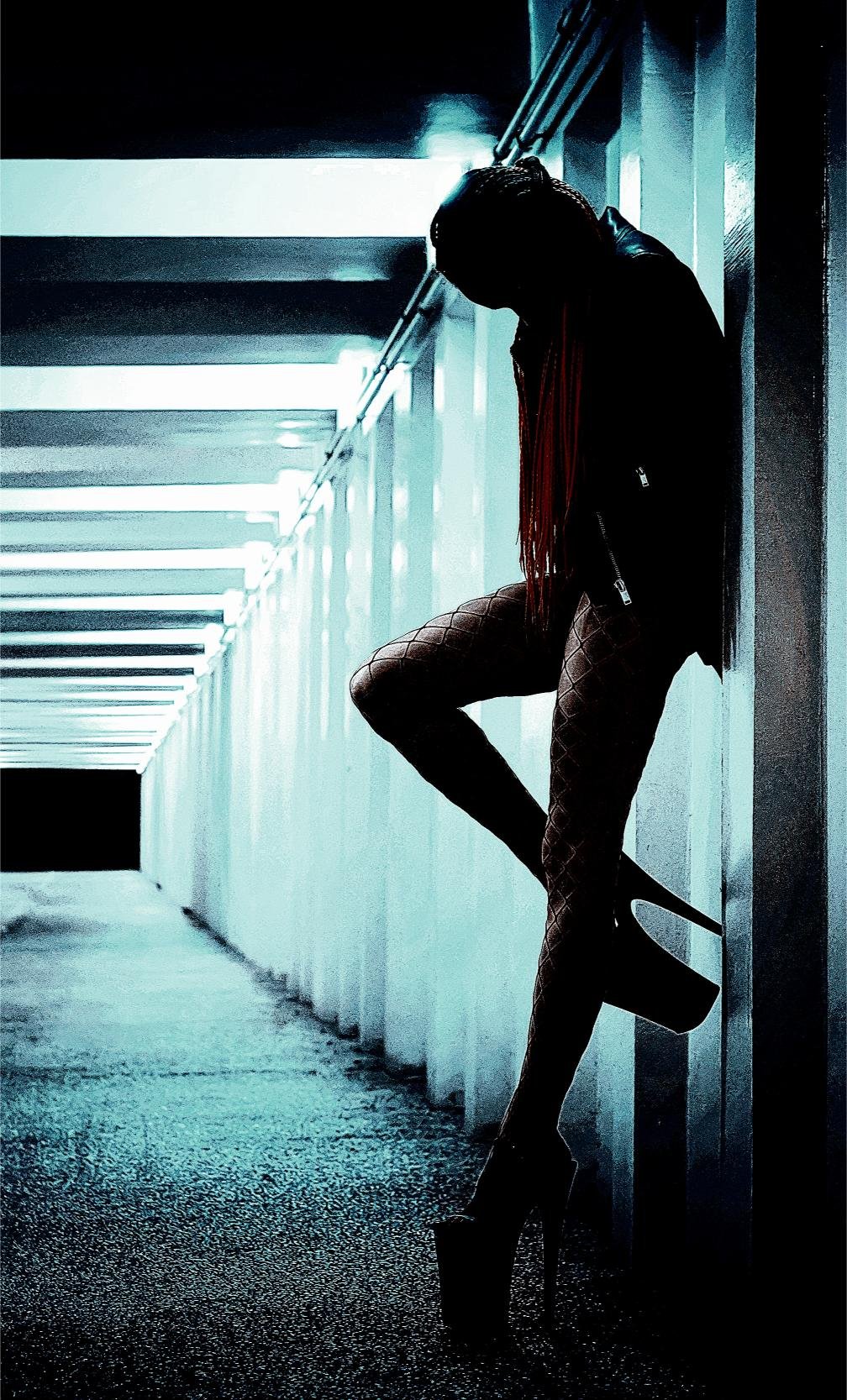 Silhouetted woman in high heels and fishnet stockings, standing in a dimly lit corridor for an urban, mysterious vibe.