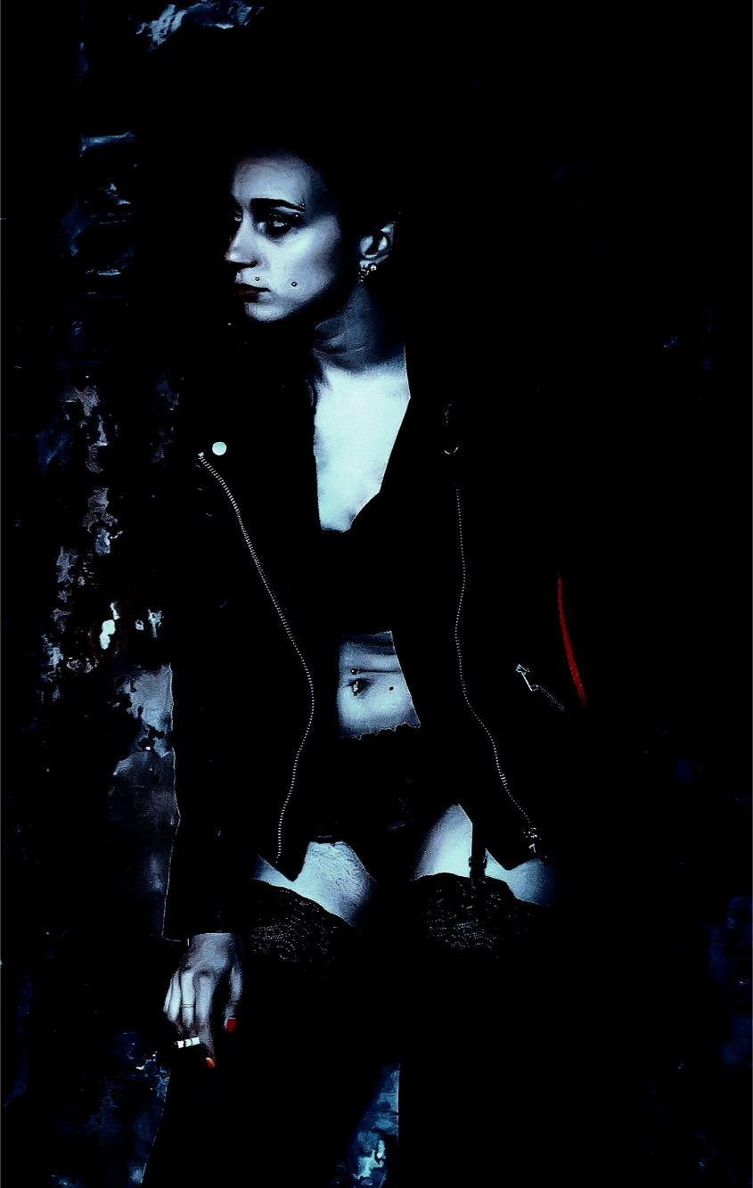Gothic woman in dark clothing with piercing gaze, framed in shadows for a mysterious, intense aesthetic.