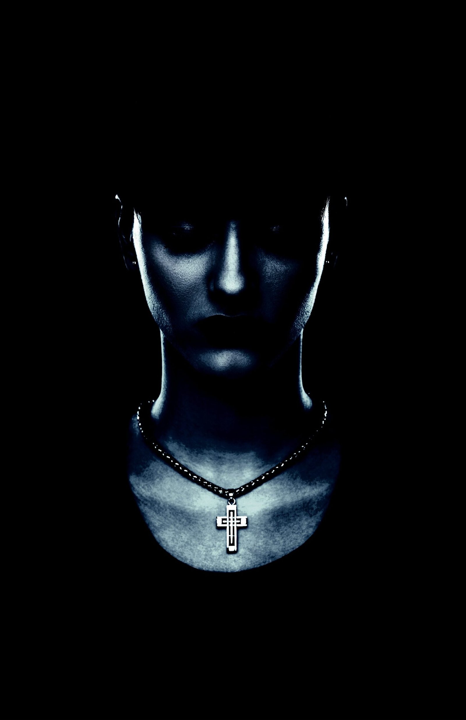 Mysterious close-up of a person wearing a gothic cross pendant necklace in shadowy lighting, capturing a minimalist dark style.