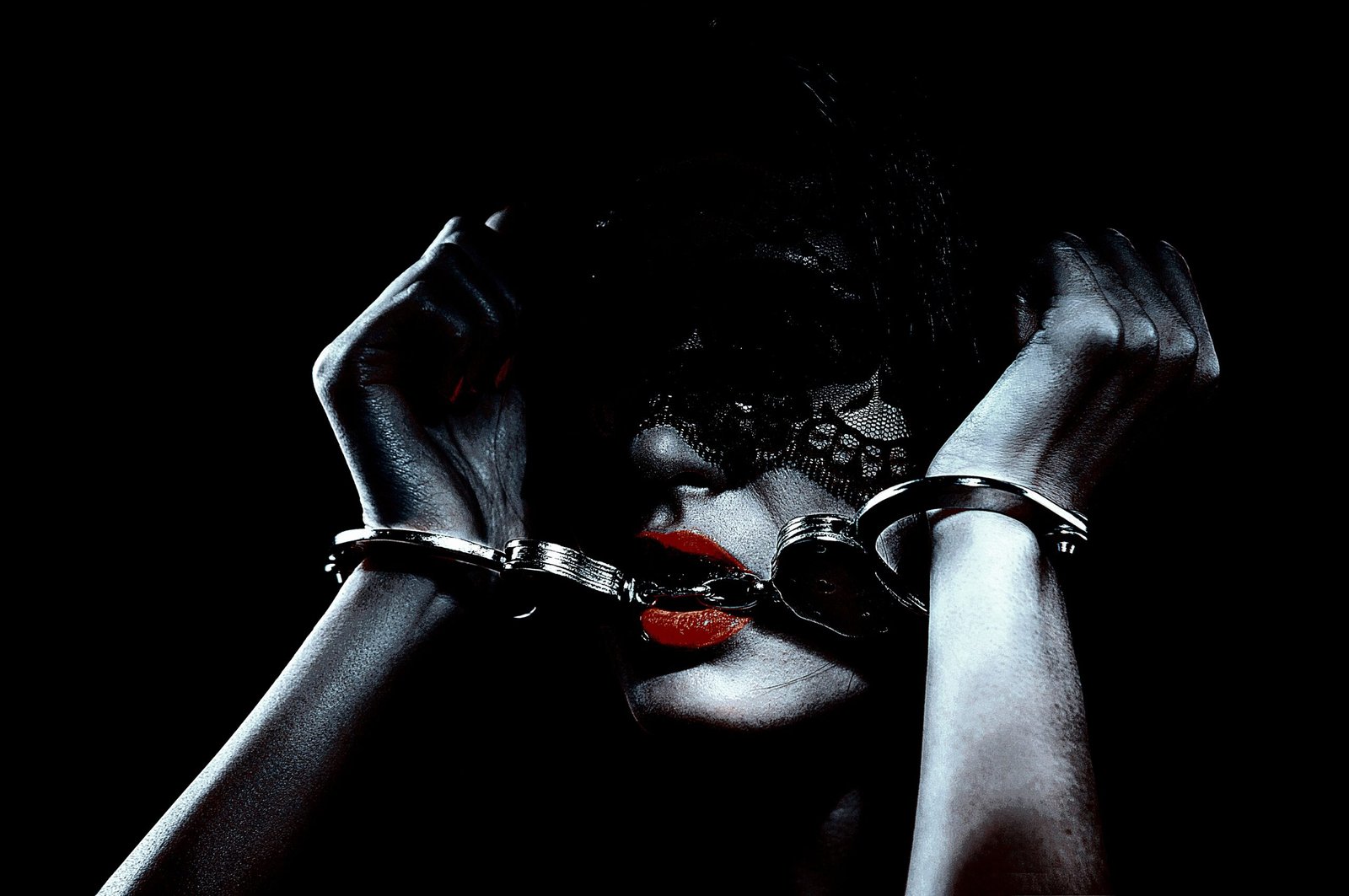 Close-up of a woman with red lips and black lace mask, holding handcuffs near her face.