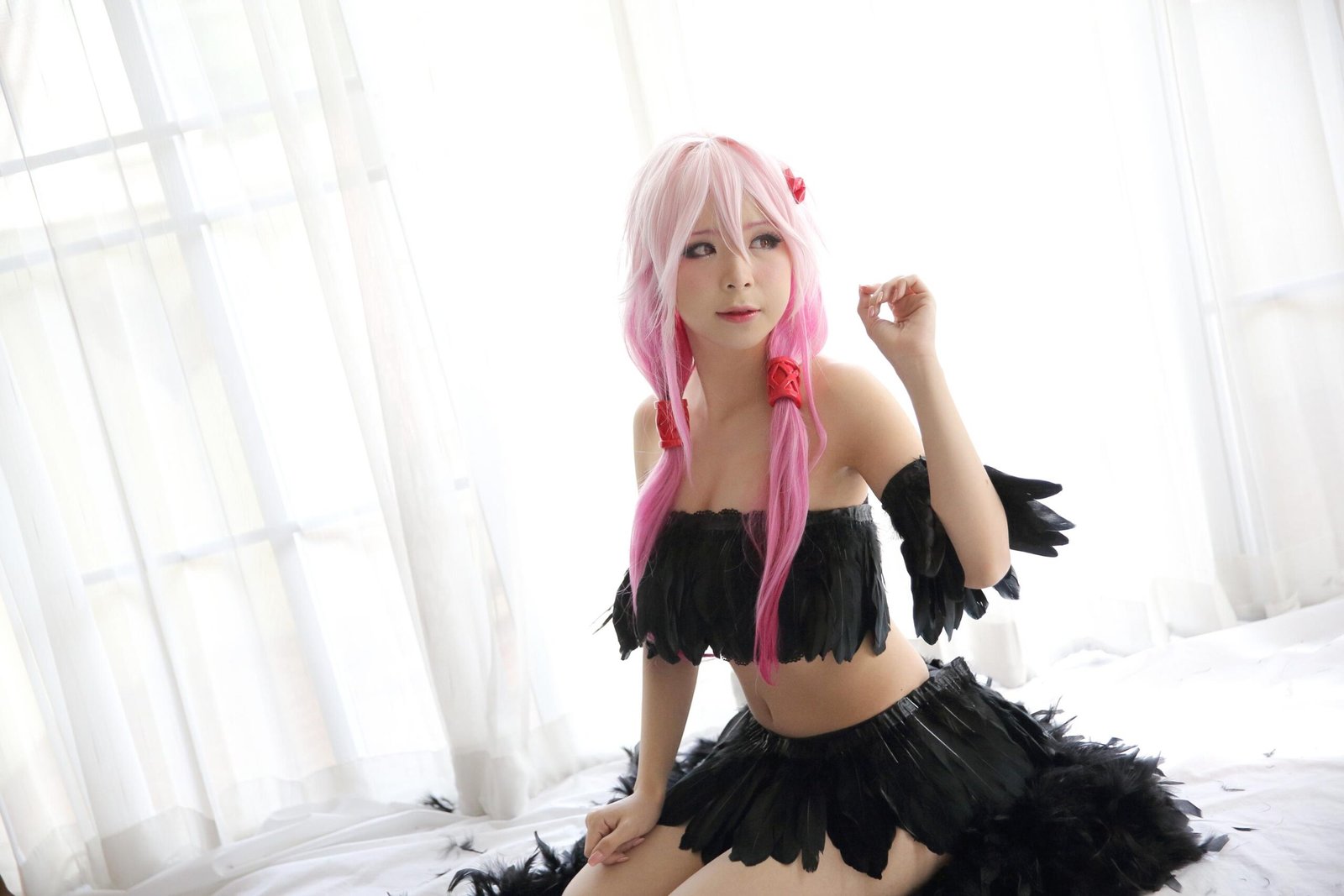 A cosplayer with pink hair styled in twin braids, wearing a black feathered outfit, sitting gracefully in a bright room with white curtains, creating a soft and whimsical scene.