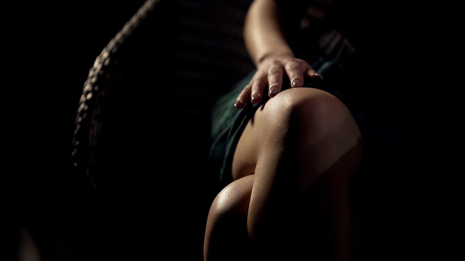 Close-up of a woman's hand resting on her knee, highlighting intimacy and softness in minimal lighting. 