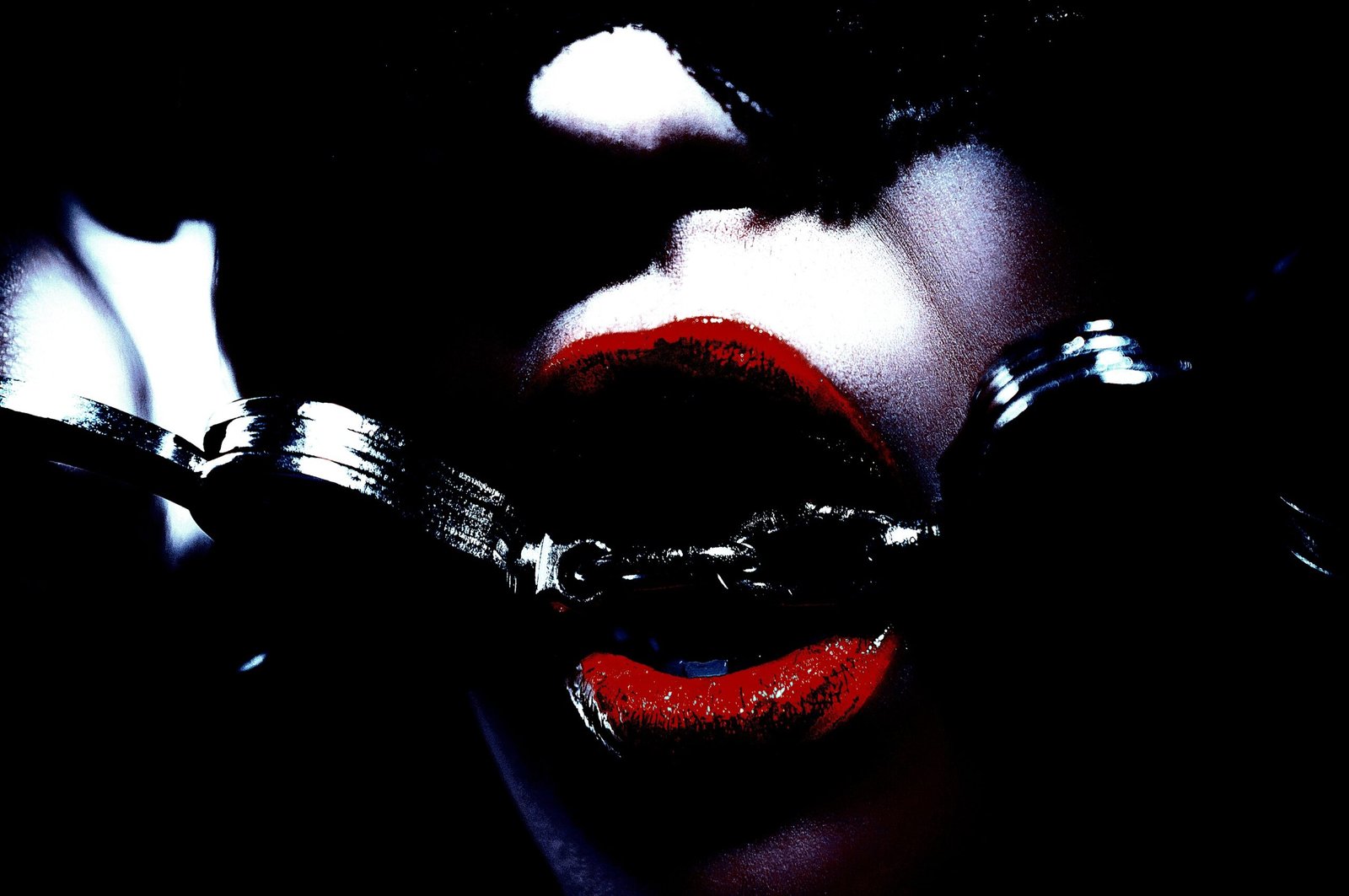 Close-up of red lips with handcuffs, partially obscured by darkness.