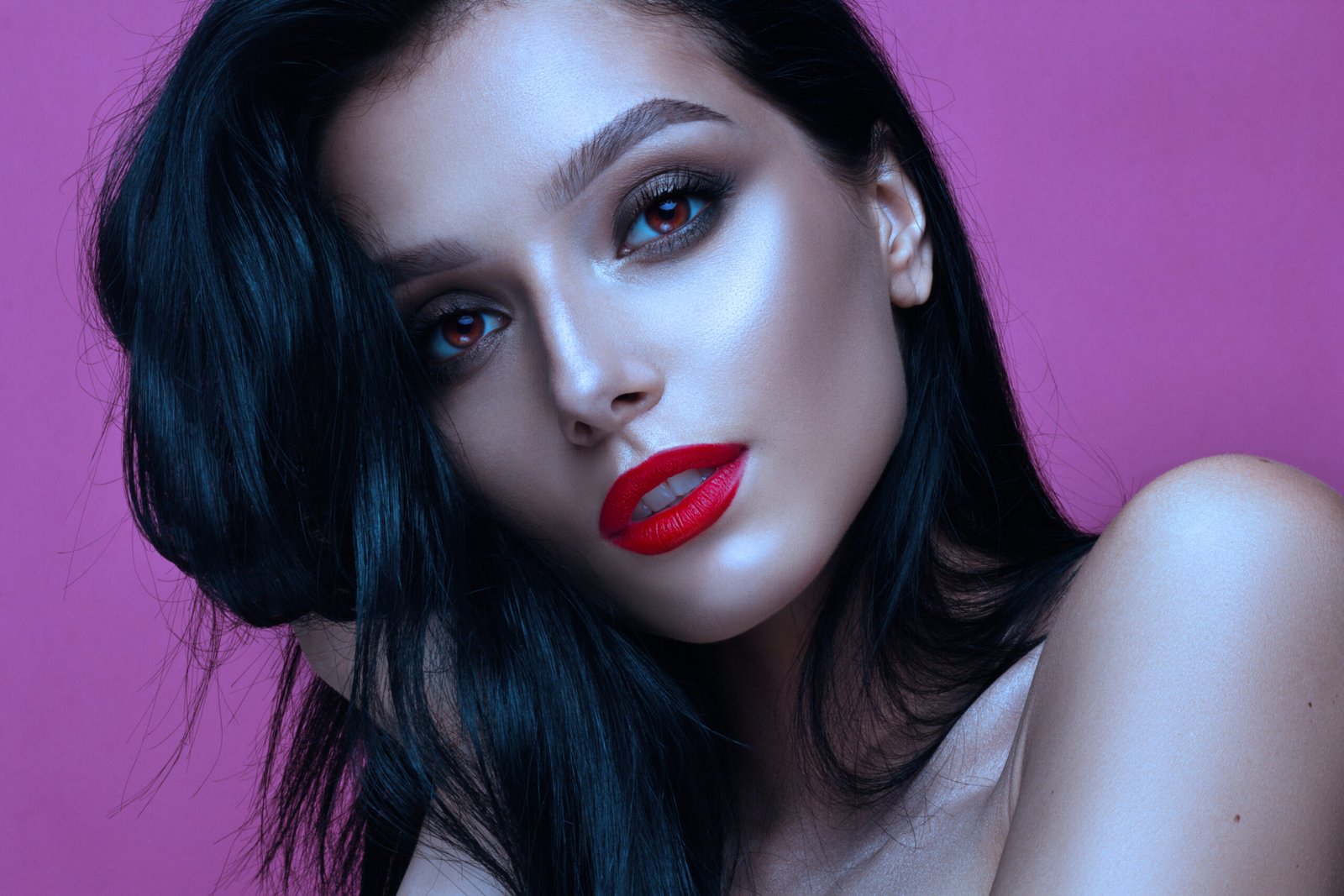 Glamorous woman with bold red lips and dark hair, posing against a pink background, representing a vampy look.
