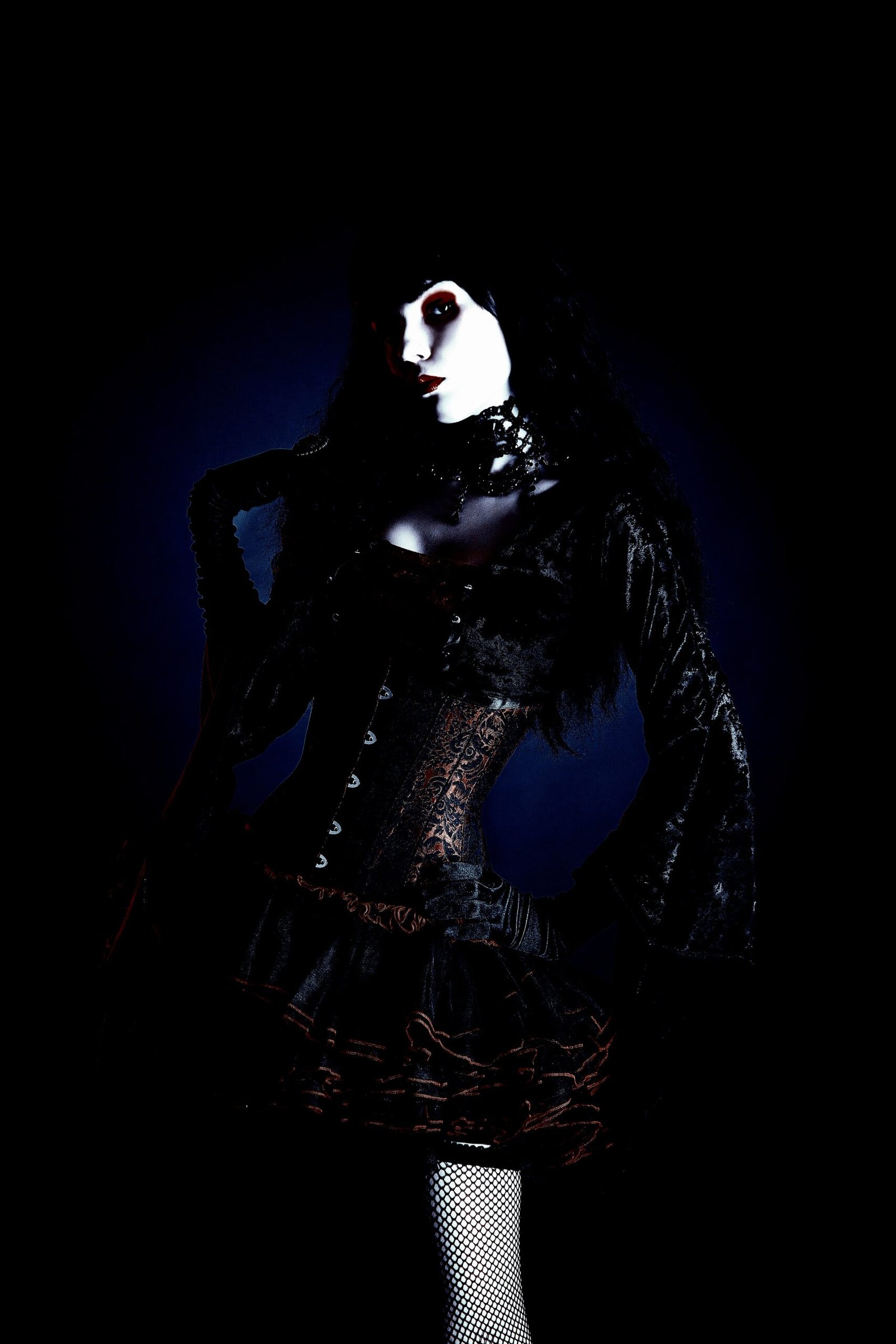Gothic woman in a corset and lace choker, illuminated by shadowy blue lighting, showcasing Victorian-inspired dark fashion.