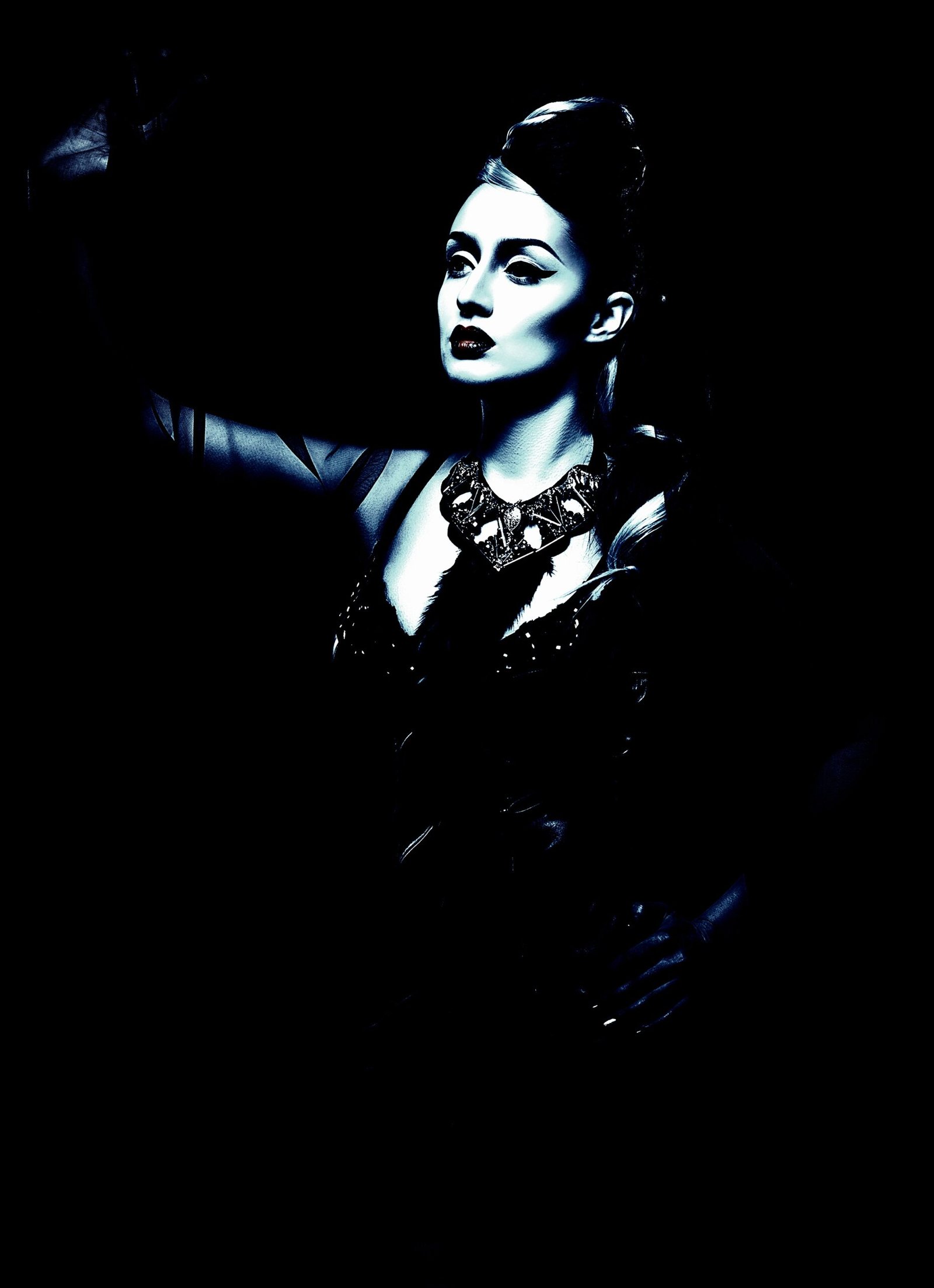 High-contrast portrait of a woman in a dramatic gothic necklace, lit in moody blue tones, capturing a hauntingly elegant aesthetic.