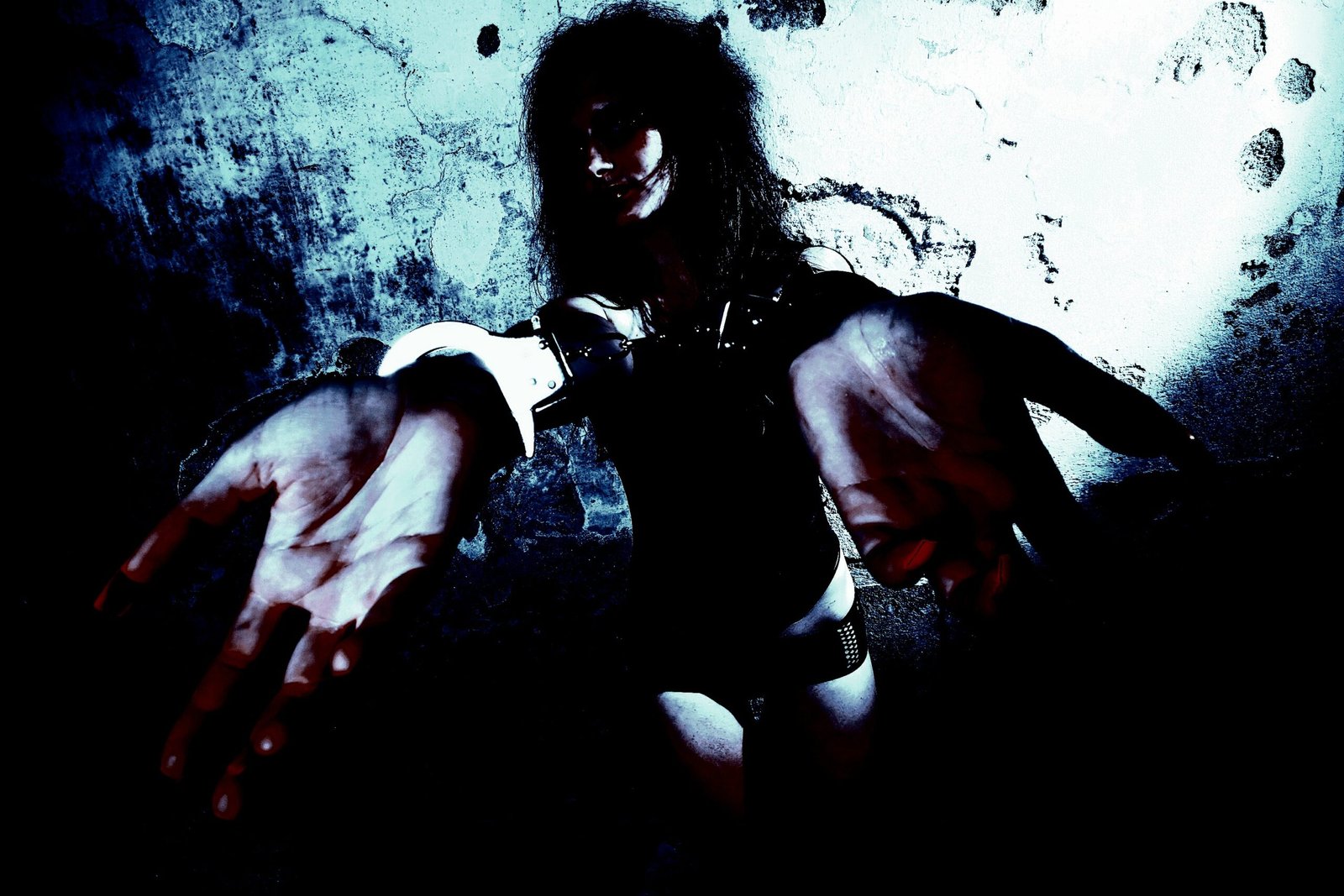 Person in black lingerie and handcuffs, reaching out with both hands in a dimly lit environment. 