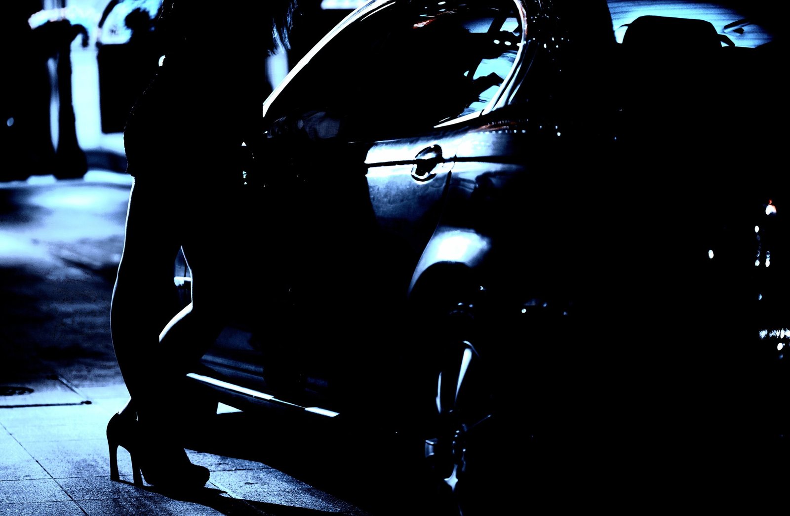 Silhouette of a person entering a car at night, highlighted against the dark background.
