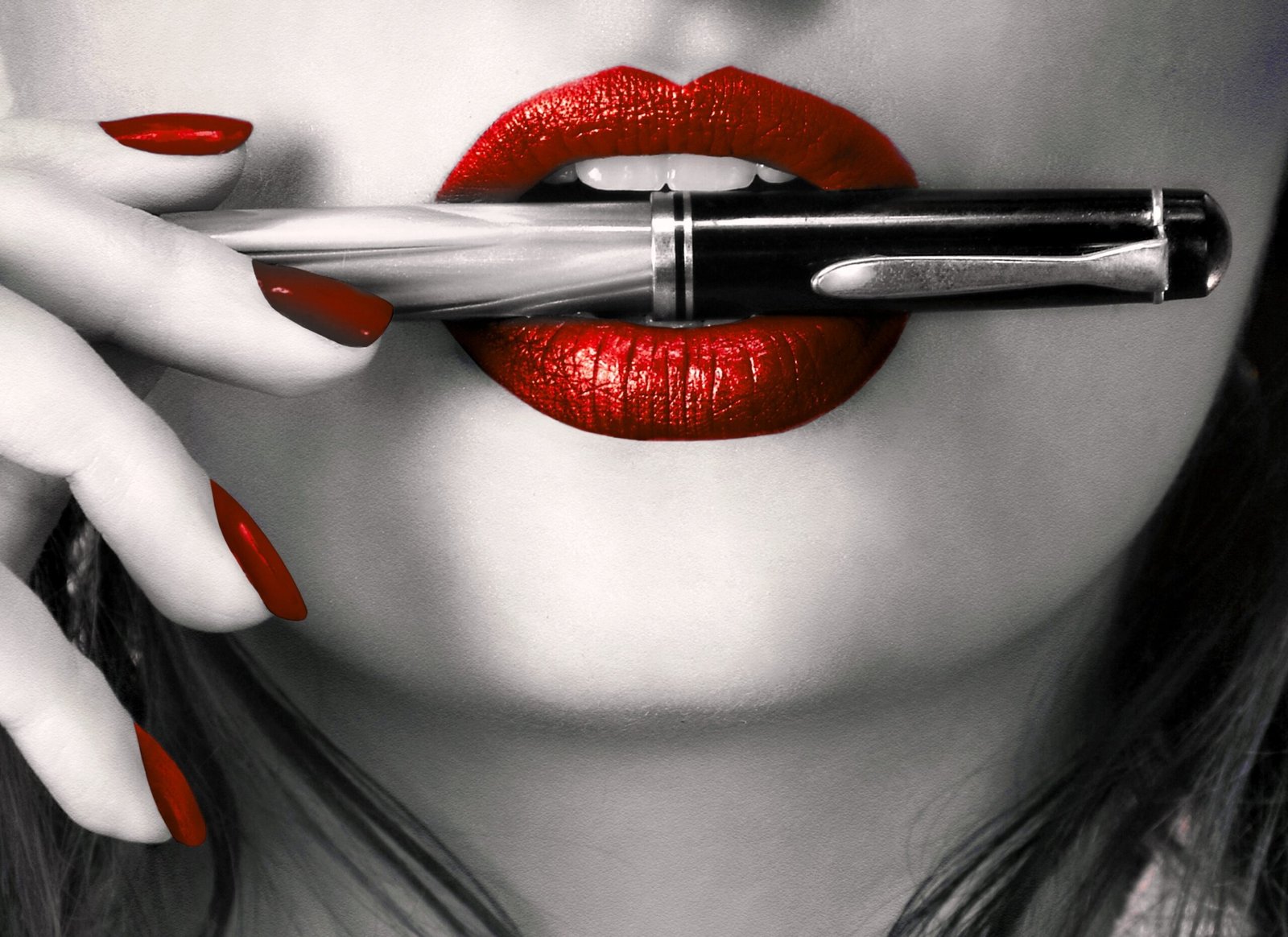 Close-up of a woman's red lips and fingers with a pen between her lips.