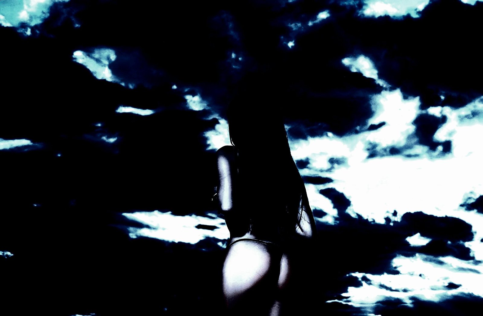 Silhouette of a woman in a thong standing against a dark, stormy night sky.